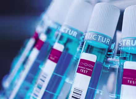 Close-up image of several test tubes with white caps and blue labels, each labeled "Biological Sample Test." The test tubes are arranged in a slanted row within a rack, and the focus is on the labels and the caps. The lighting casts a blue tint overall.