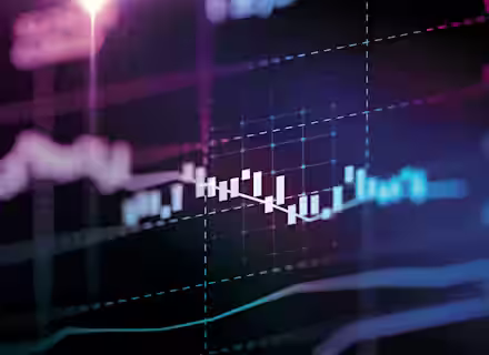 A close-up of a digital screen displaying a financial chart with candlestick patterns, grid lines, and various data lines. The background is dark, illuminated by colorful lights and gradients, creating a dynamic and futuristic feel.