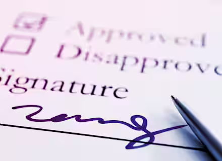 A close-up of a form with two checkboxes labeled "Approved" and "Disapproved." The "Approved" box is checked. Below is the word "Signature" with a cursive signature and a pen resting on the paper. The image is lit with a purple hue.