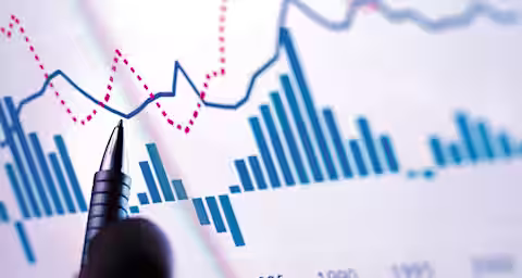 A hand holding a pen is pointing at a multi-colored graph on a screen. The graph shows various lines and bar charts, depicting data trends from 1980 to the 2000s. The main colors used are blue, red, and pink, indicating different data series.
