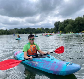 Smiling dark haired boy in sunglasses paddling blue kayak on Stanborough Lake