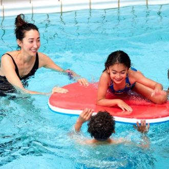 An image of a parent with her two kids (trying to climb onto a swimming float)