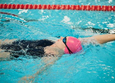 female with pink hat doing backstroke in a lane pool