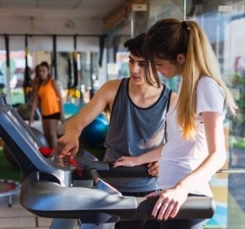 Junior Induction - fitness instructor in gym instructing girl on exercise machine