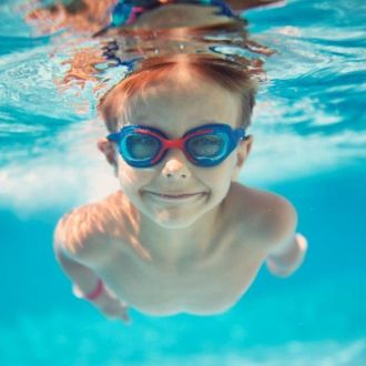 image shows young boy swimming under water with goggles on looking straight at the camera