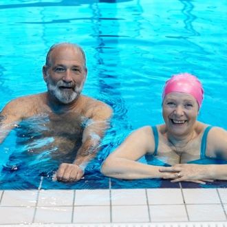 image shows an older lady and man at the edge of a pool smiling