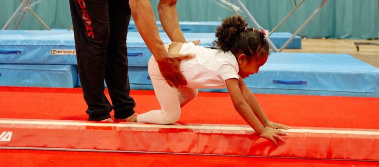 image shows a man supporting a young girl on a beam for gymnastics