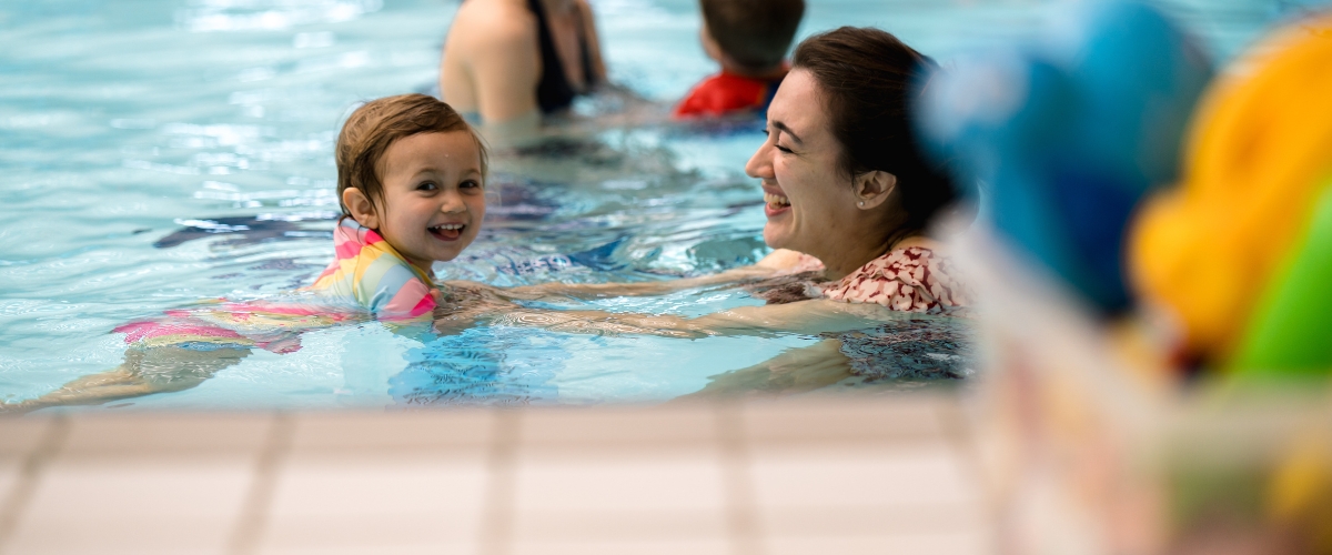 Baby swimming with her mother and smiling 