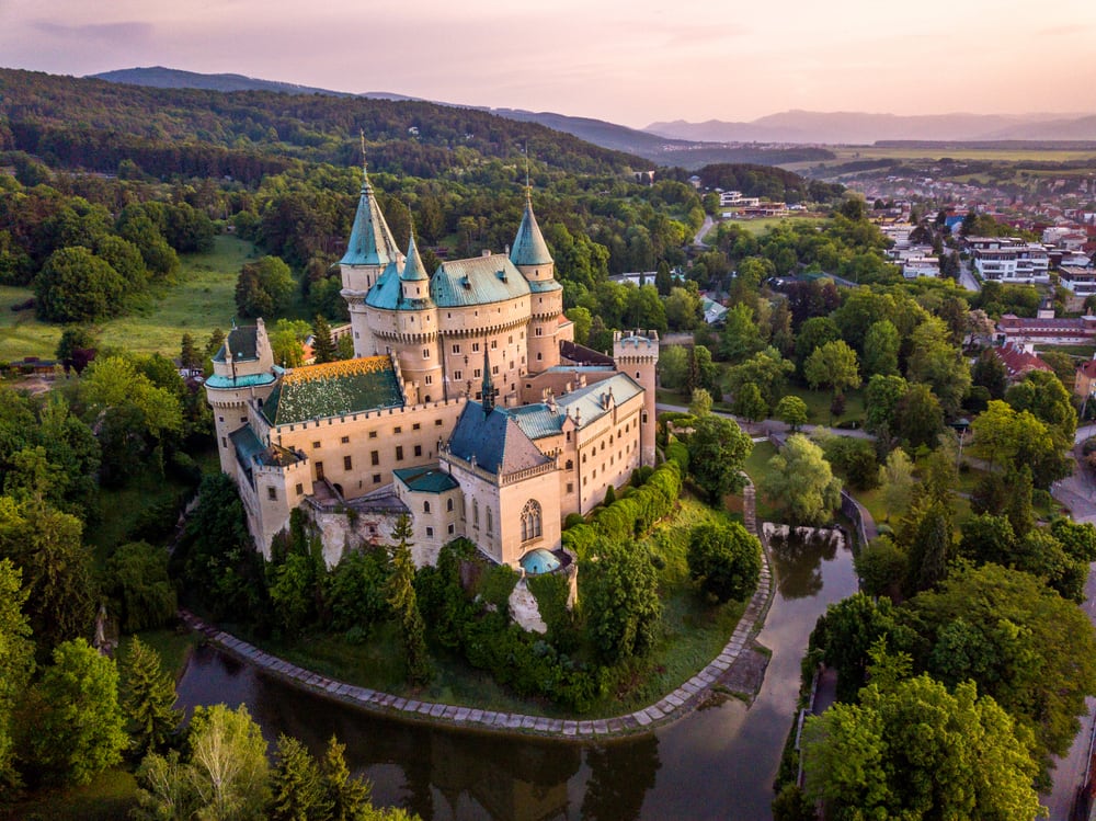 A Pink Castle on a Hillside Surrounded by Trees at Sunset