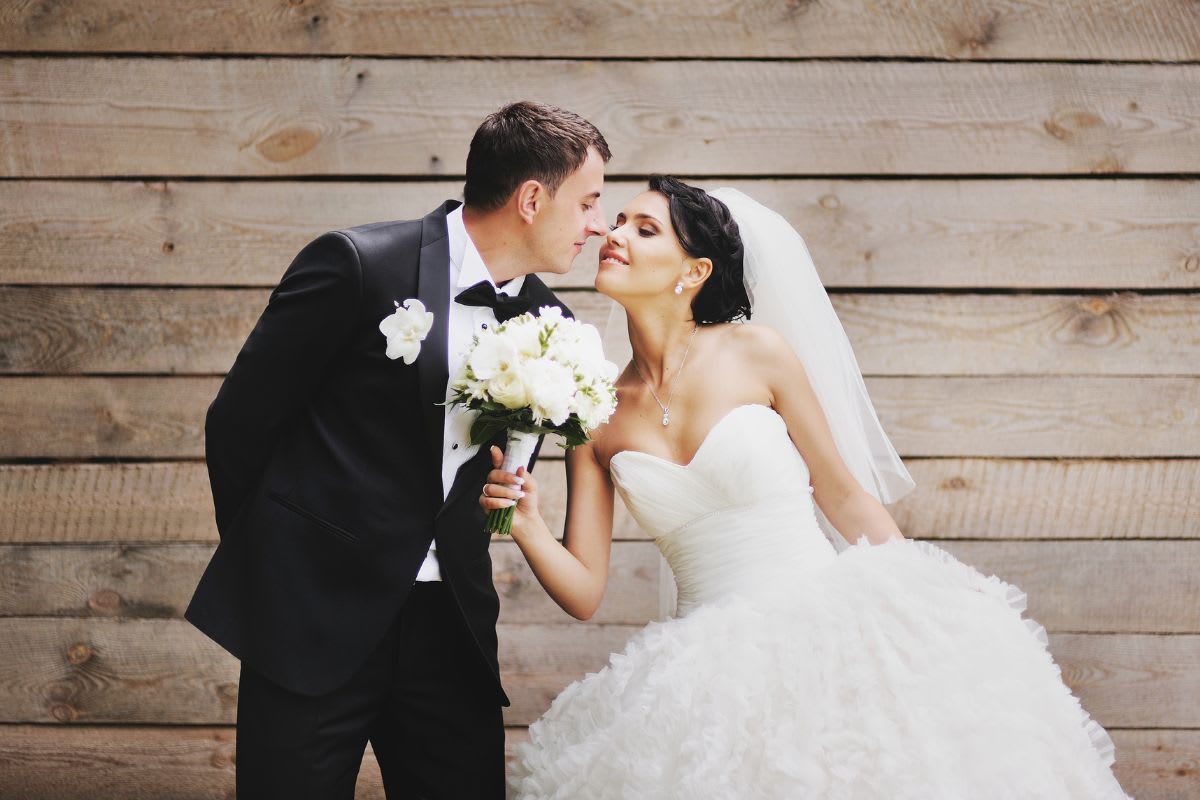 Brautpaar küsst sich liebevoll, umgeben von einer Holzkulisse, die die intime und persönliche Natur einer dänischen Hochzeit widerspiegelt.