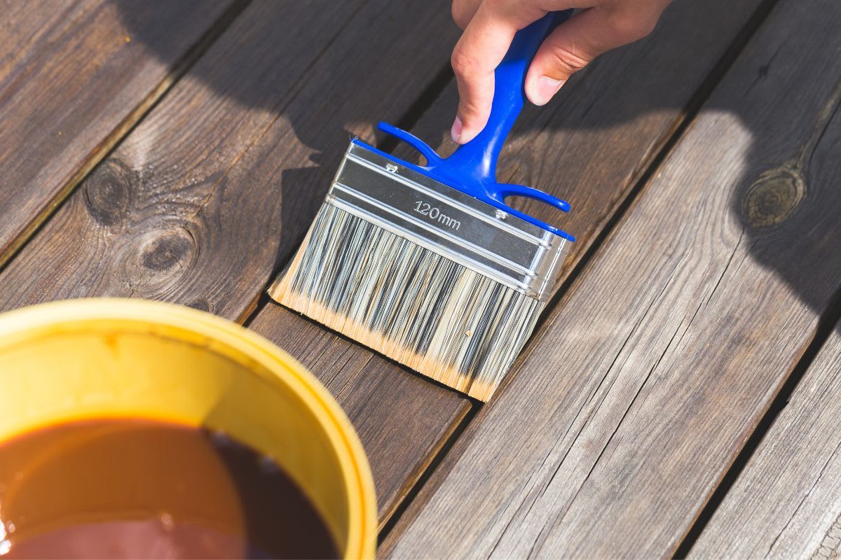Anwendung von Holzschutzlasur auf Terrassendielen mit einem Pinsel zur langfristigen Pflege und Erhaltung der natürlichen Holzschönheit.