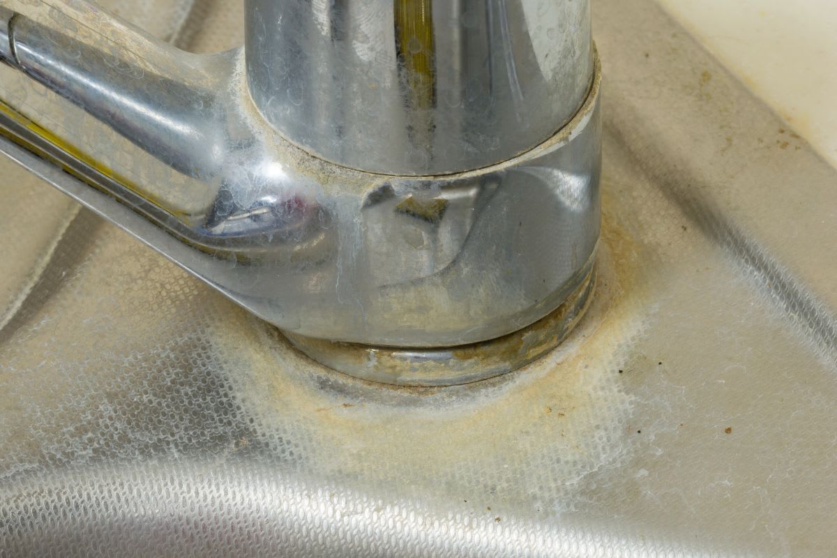 Hartnäckige Kalkablagerungen um den Sockel eines Wasserhahns auf einer Spüle.