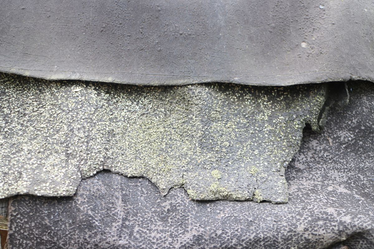 Alter, abgenutzter und teilweise abgelöster Abschnitt von Dachpappe mit sichtbarem Moosbewuchs auf der Oberfläche.