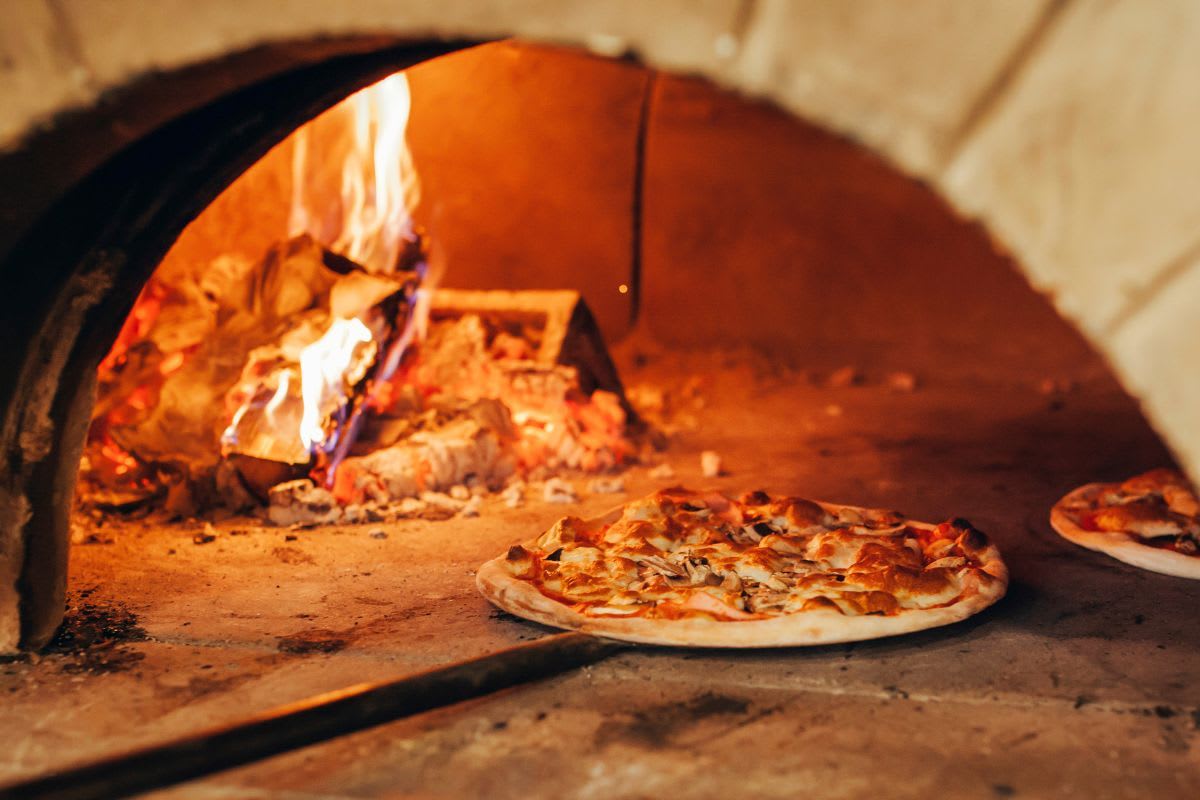 Pizza im Inneren eines traditionellen Steinofens, beleuchtet von den Flammen des Feuers.