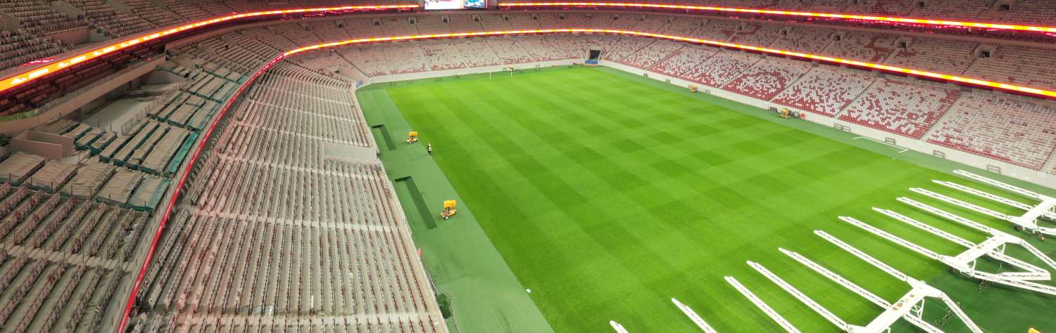 Wide-angle view of an empty modern sports stadium with a green grass field and a large circular opening in the roof.