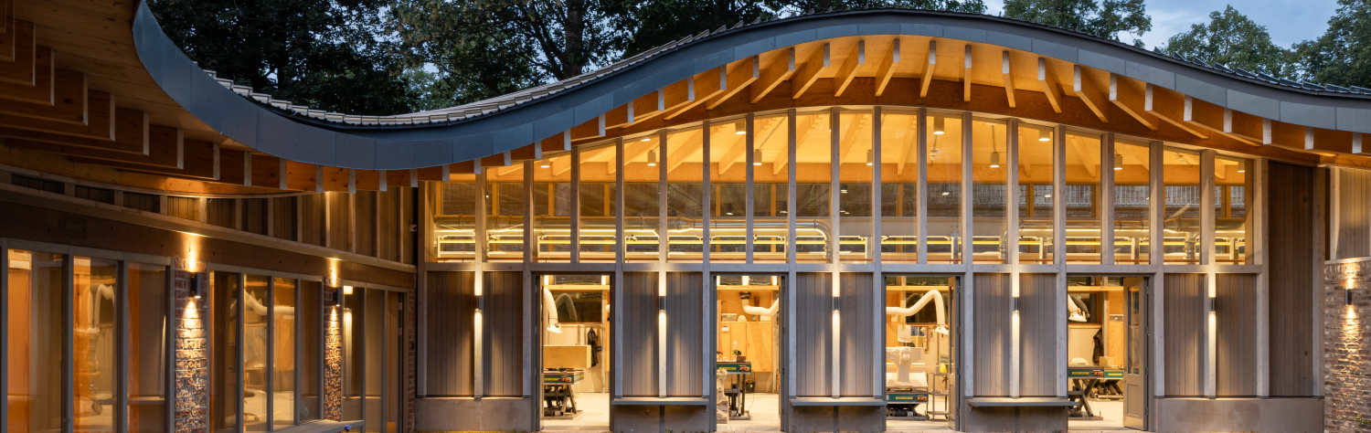 Modern building with a curved wooden roof and large glass windows overlooking a paved courtyard.