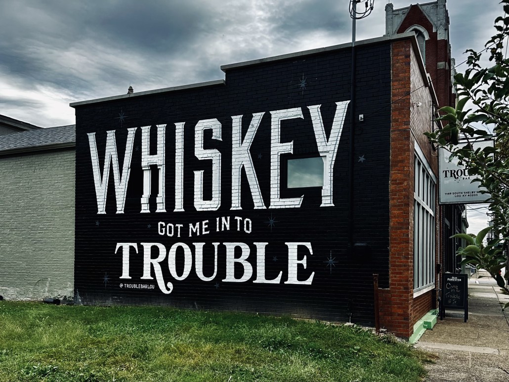 A sign on the side of a Louisville building reads Whiskey Got Me Into Trouble