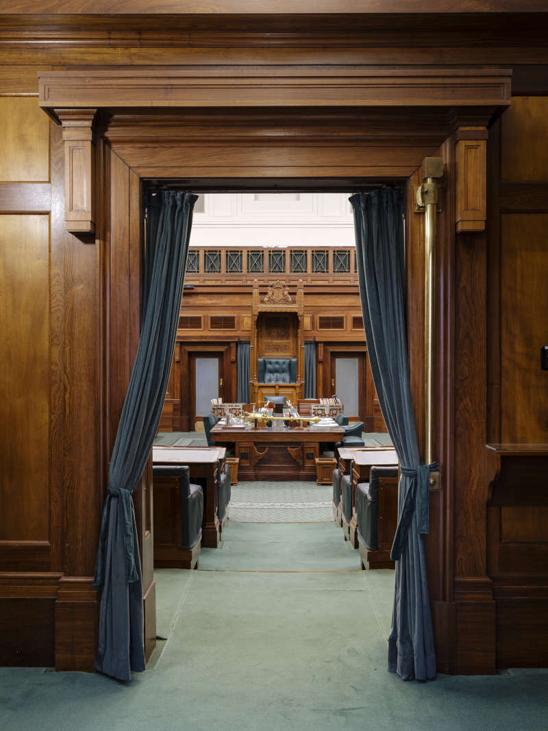 Looking into the green House of Representatives chamber with its ornate curtains, timber panelling and a view of the Speaker's Chair.