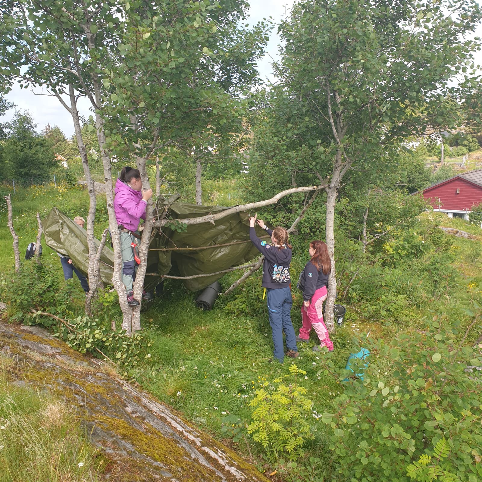 Fire unge speidere lager ly for regnet ved hjelp av grener og presenning. Samhold, mestring og samarbeid er grunnverdier for Øygarden Speidargruppe.