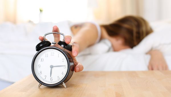woman in bed shutting off alarm clock