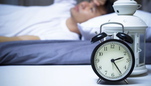 man laying in bed next to alarm clock