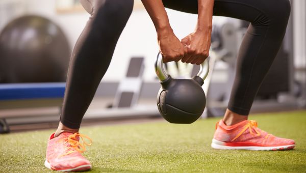 Woman exercising with a kettlebell weight, low-section crop