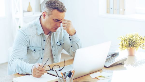 Frustrated mature man looking exhausted while sitting at his working place and carrying his glasses in hand