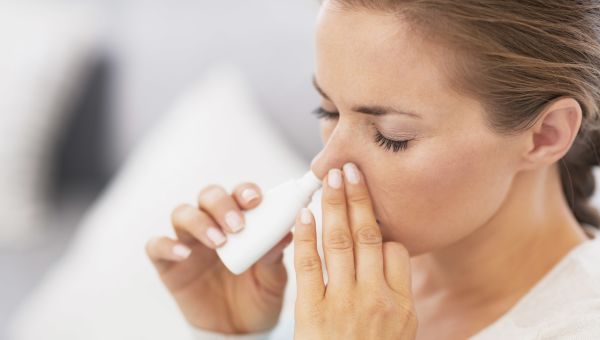 woman putting nasal spray in her nose