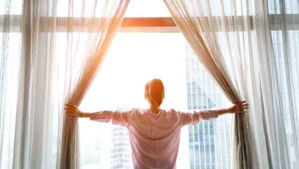 Young woman opening up her curtains