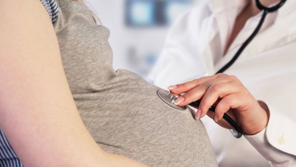 Doctor listening to pregnant person's abdomen with a stethoscope