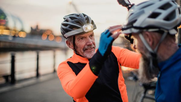 Senior man wearing a bicycle helmet adjusting another man's bicycle helmet
