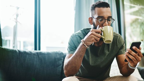 Man sipping a cup of tea while on this phone.