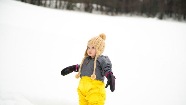 Asian baby dressed in coat, snow pants, hat and gloves in the snow