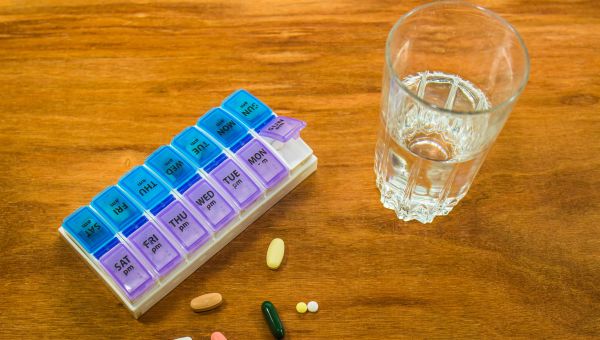 Medications and pill box with glass of water.