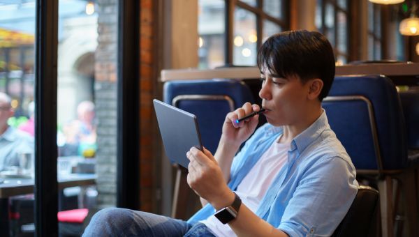 A young Asian man smokes an e-cigarette in a cafe.