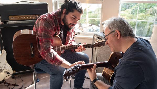 a young man teachers an older man how to play acoustic guitar