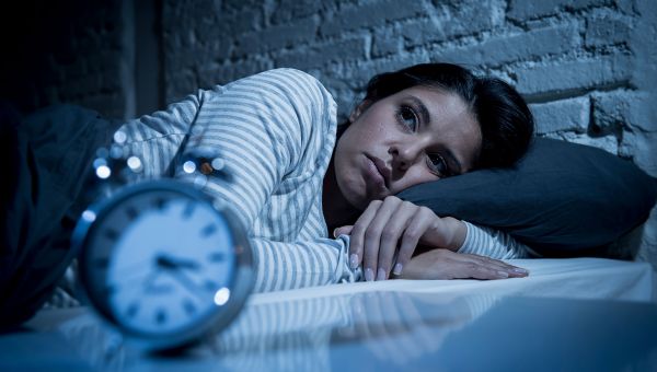 Woman lies awake in bed with clock nearby.