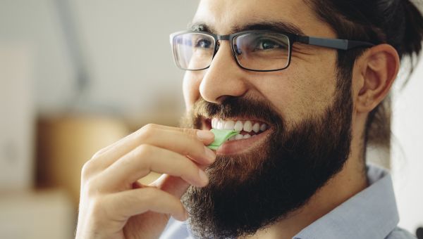 a young man with a beard and glasses chews some sugar-free gum