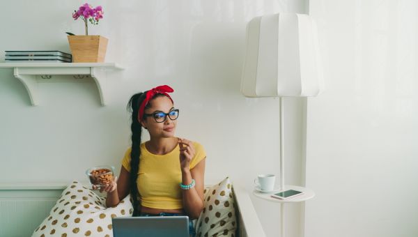 woman at home computer wearing glasses and eating nuts
