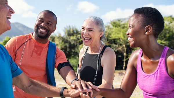 Diverse group of four people wearing colorful exercise clothes, standing in a circle and smiling while doing a group high five