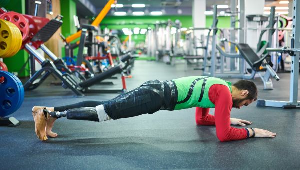 Young man with a prosthetic leg holding a plank pose in the middle of a gym.