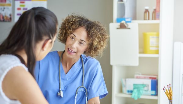 a friendly Black nurse speaks with a female patient about her pregnancy