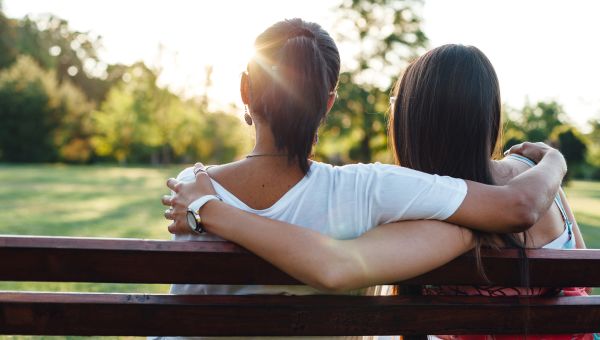 Couple snuggles on bench in park.