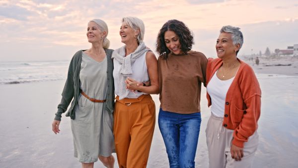 Four people walking together on a beach with their arms around each other