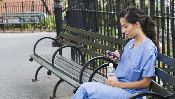 a nurse in blue scrubs sits on a park bench with a bottle of water to drink