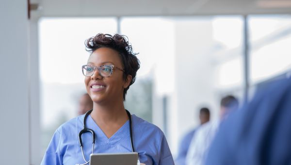 a Latina nurse in blue hospital scrubs looks up from her work tablet and smiles
