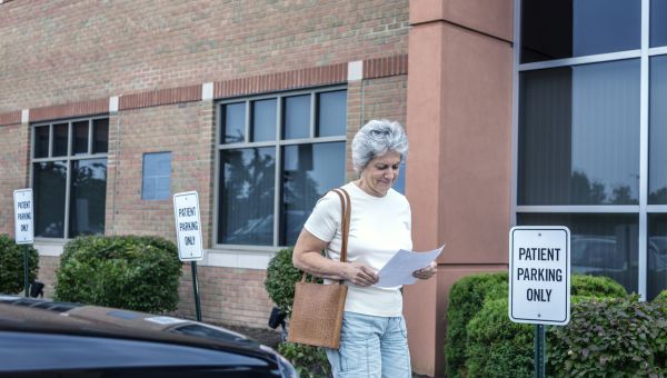 an older white woman walks from a parking lot to a doctor's office