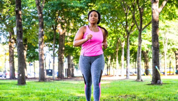a young overweight Black woman in sporty workout wear runs in the park