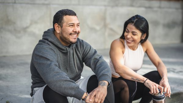 a Latino couple, man and woman, in workout wear sit on a curb and chat after exercising