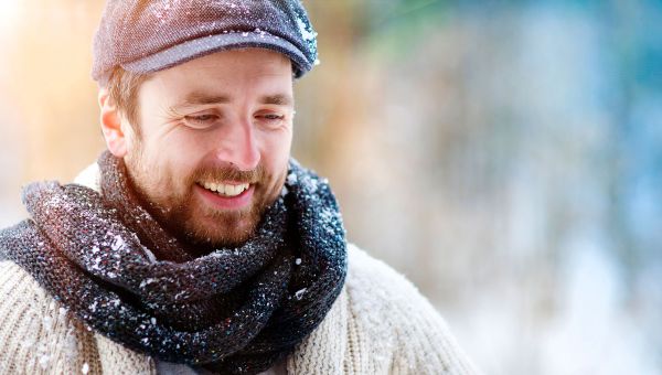 Man smiles wearing a cap and standing outside.